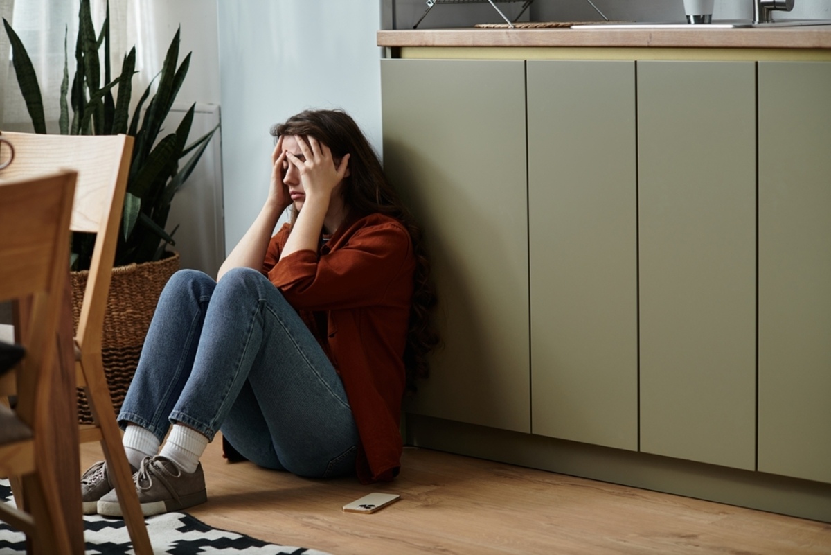 Woman with high-functioning depression sitting alone on the floor holding her head