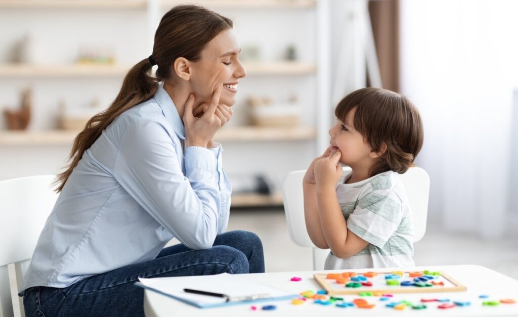 A clinician smiling and engaging with a young boy during an evaluation session to identify signs of autism in children using colorful sorting toys