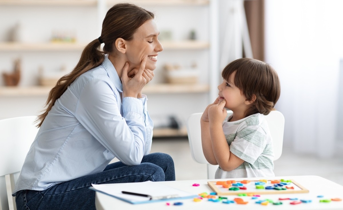 A clinician smiling and engaging with a young boy during an evaluation session to identify signs of autism in children using colorful sorting toys